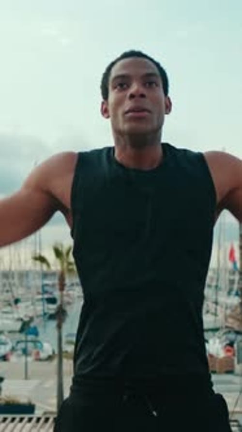 Vertical video, Fit Black Man Doing Jumping Jacks by the Marina
