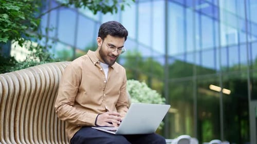 Man Cheers Using Laptop on Bench Outdoors