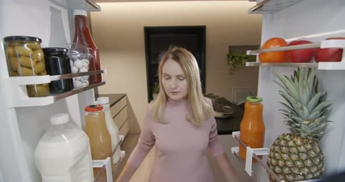 A Middleaged Woman Takes a Container of Food Out of the Refrigerator View From Inside the