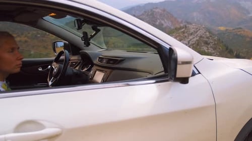 Young woman blonde sits in an off-road car admiring the beauty of the mountain landscape