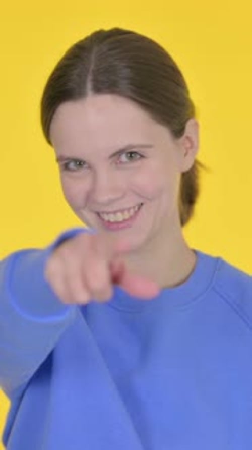Jeune femme pointant vers la caméra sur fond jaune, vidéo verticale