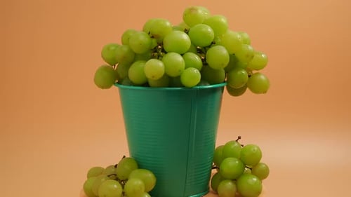 Rotating green grapes. Ripe grapes in a bucket on an orange background. Close-up.