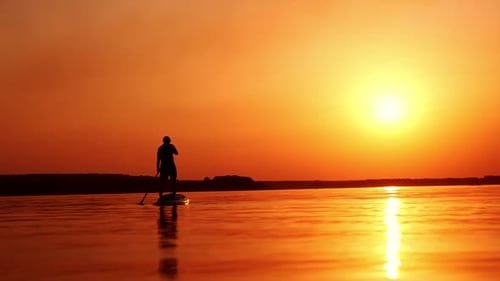 Black male silhouette of a sportsman practicing sup boarding. Man holding a paddle rowing with it.