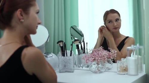 Woman Puts On Earring in Front of Mirror