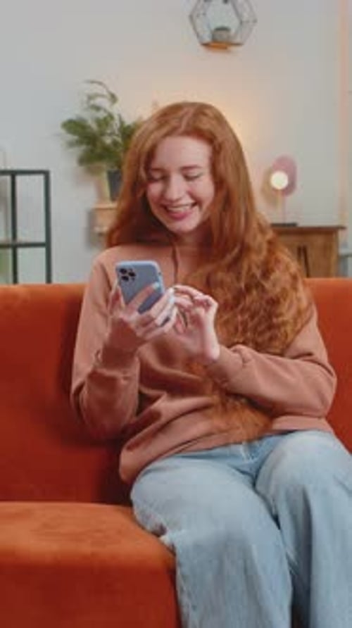 Smiling Woman Using Smartphone on Orange Sofa