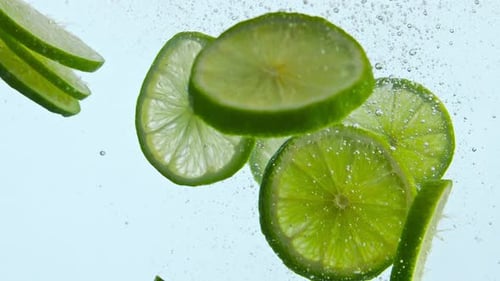 Fresh green lime slices floating underwater with bubbles in super slow motion