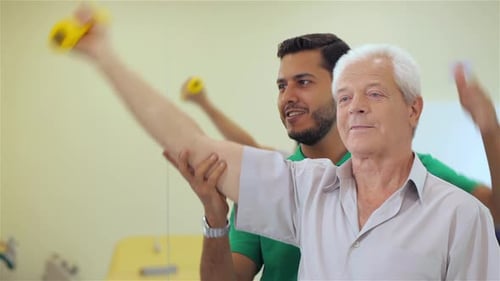 Senior Man Lifts Up the Dumbbell at the Hospital