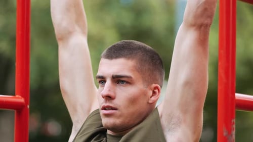 Focused young athletic man doing pull-ups at red sports facility in park