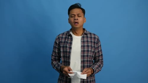 Man Sneeze into Tissue Against Blue Background