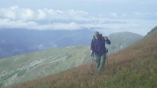 A man with a backpack climbs the mountain, conquers the top of the mountain