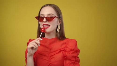 Une femme chic vêtue d'une robe rouge éclatante, de lunettes de soleil élégantes et d'une sucette respire la confiance