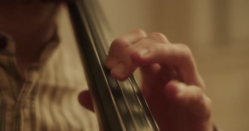 Close up shot of the left hand of a cellist moving over the strings of a cello, doing vibrato with t