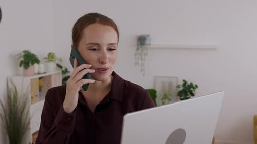 Young Businesswoman Talking on Phone While Working on Laptop at Modern Office