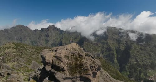 Athletic woman steps onto top of mountain summit on sunny day raising arms in air