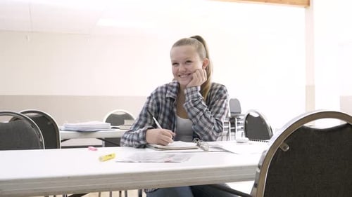Happy high school student smiling attentively doing homework at classroom table