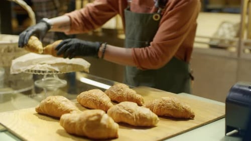 Close Up of Saleswoman Putting Fresh Croissants on Glass Cake Stand in Bakery