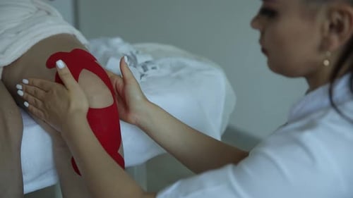 Woman Applies Red Kinesiology Tape to Patients Knee