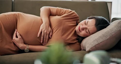 Magenschmerzen, Schwangerschaft und Symptome bei Krankheit, Müdigkeit und Mutterschaft bei einer Frau auf dem Sofa