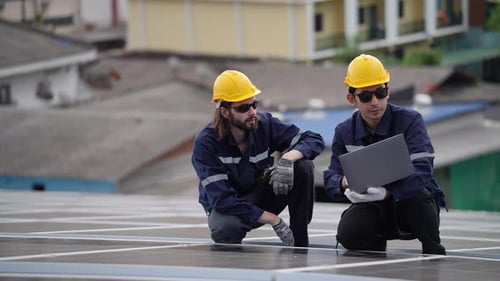 Solar Panel Workers Inspecting Rooftop Installation with Laptop