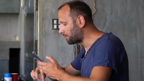 Man Eating and Using Mobile Phone Indoors