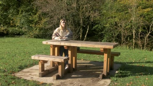 A woman writes at a park bench in nature. WIDE SHOT