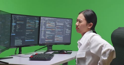 Asian Woman Developer Having Backache While Write Code With Multiple Screens In Green Screen Studio