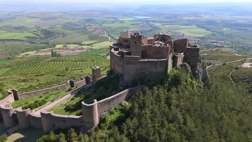 Drone orbiting medieval castle on rocky hill surrounded by green valley and rural landscape