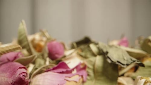 Scattered dry tea leaves with chamomile and rose petals on the table. Dolly slider extreme close-up.
