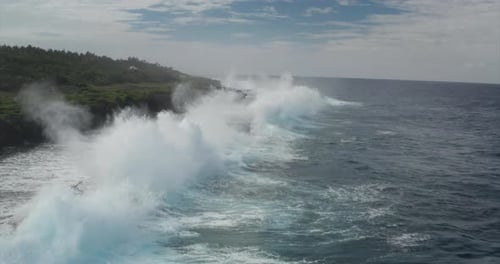 Aerial shot of sea waves are crashing into the rocky cliffs of a desert island before the storm.