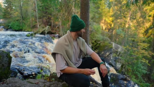 Ruhe in der Natur Der Mensch sitzt alleine in der Naturlandschaft mit kleinem Fluss und genießt Ruhe und Wasser