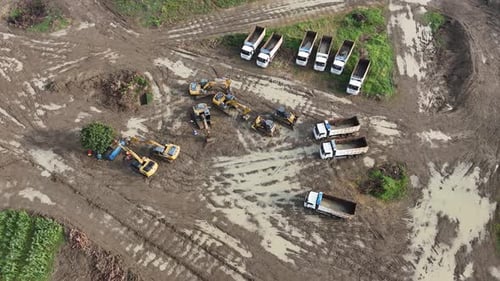 Aerial Perspective of Construction Site Featuring Heavy Machinery and Transport Trucks Amidst a Mudd