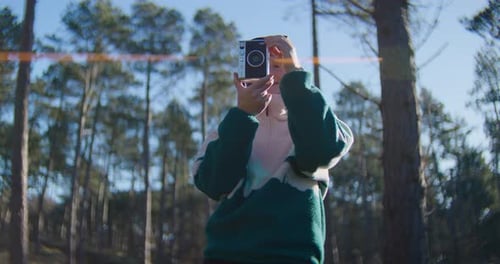 Woman taking photos in woods on sunny day