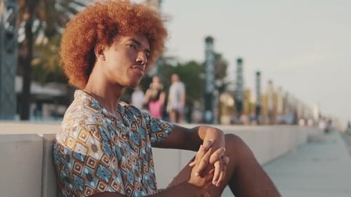 Portrait of young man sitting outdoors in the city against palm trees and buildings background