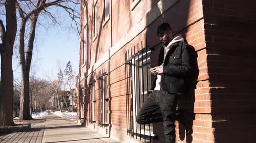 Young Man Using Smart Phone Against Sunny Urban Brick Building Adult