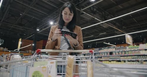 Young Woman Supermarket Customer Choosing Food Putting Product in Trolley Shopping in Retail Store