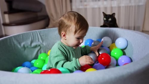 Beautiful baby boy sitting in the basin with bright colorful plastic balls.