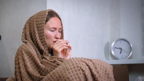 Femme essayant de se réchauffer assise enveloppée dans une couverture à la maison sans chauffage