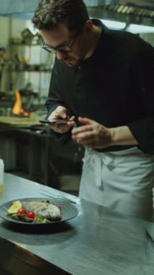 Chef Photographing Fish Served on Plate with Phone in Restaurant Kitchen