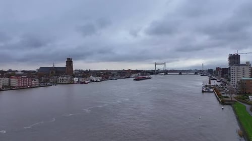 In distance, silhouette of container vessel sailing past Dordrecht city