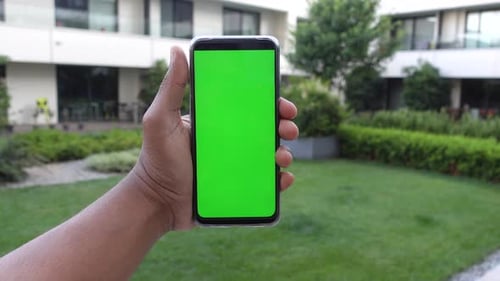 Young Man Hand Using Smart Phone with Green Screen Against City Buildings