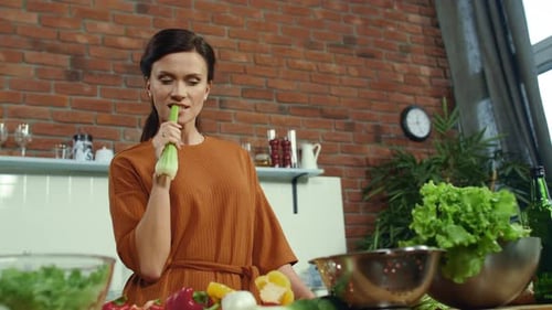 Jeune femme dégustant du céleri frais dans la cuisine. Femme au foyer souriante appréciant le céleri vert