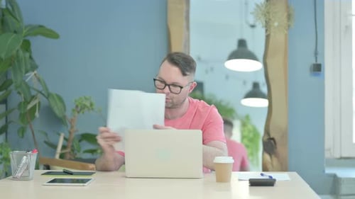Man Works at Desk with Laptop and Paperwork