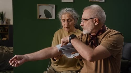Senior Woman Measures Blood Pressure of Man in Home