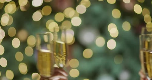 Pessoas tilintam óculos contra o pano de fundo de luzes embaçadas da árvore de Natal, festa de Ano Novo