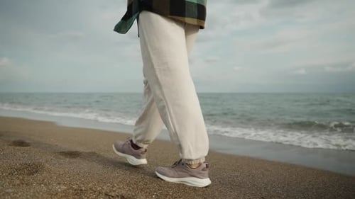 A young woman walks along the beach by the sea in cloudy and windy weather, slow motion. Rear view,
