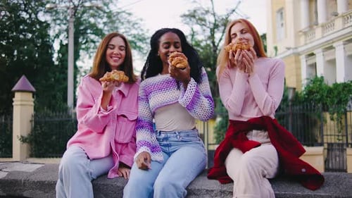 Three Smiling Friends Enjoy Croissants in City