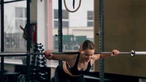 in the Gym Girl Trainer in a Black Top is Standing Doing Exercises with a Barbell