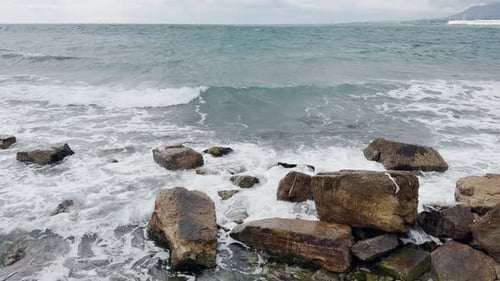 Wellen brechen an einer felsigen Küste und verkörpern die rohe Kraft des Meeres vor dem Hintergrund eines