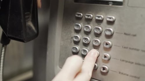 White girl is dialing nine one one from a public grey phone booth in London UK at night