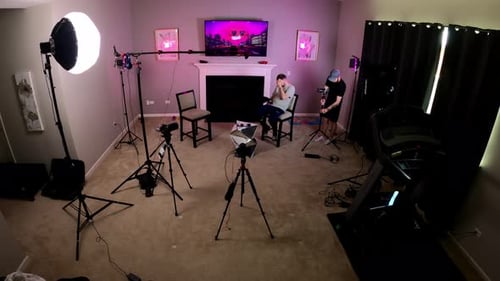 Wide view of two videographers setting up camera equipment indoor for a two person interview. Workin